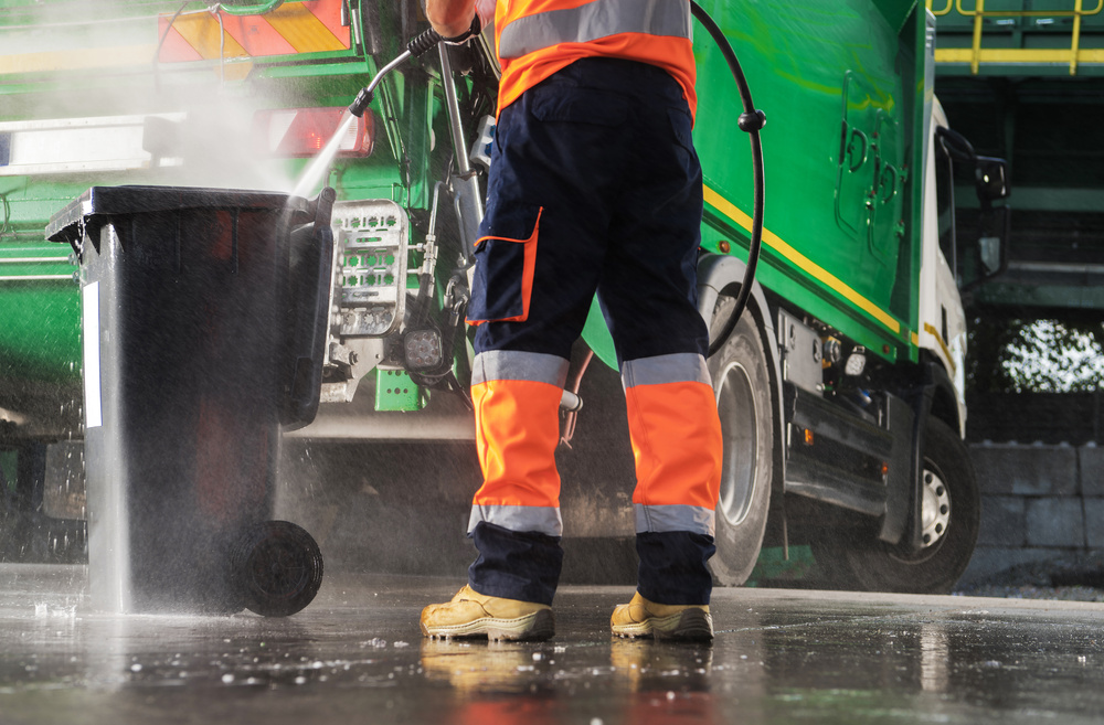 Garbage Truck Operator Pressure Washing Black Trash Can